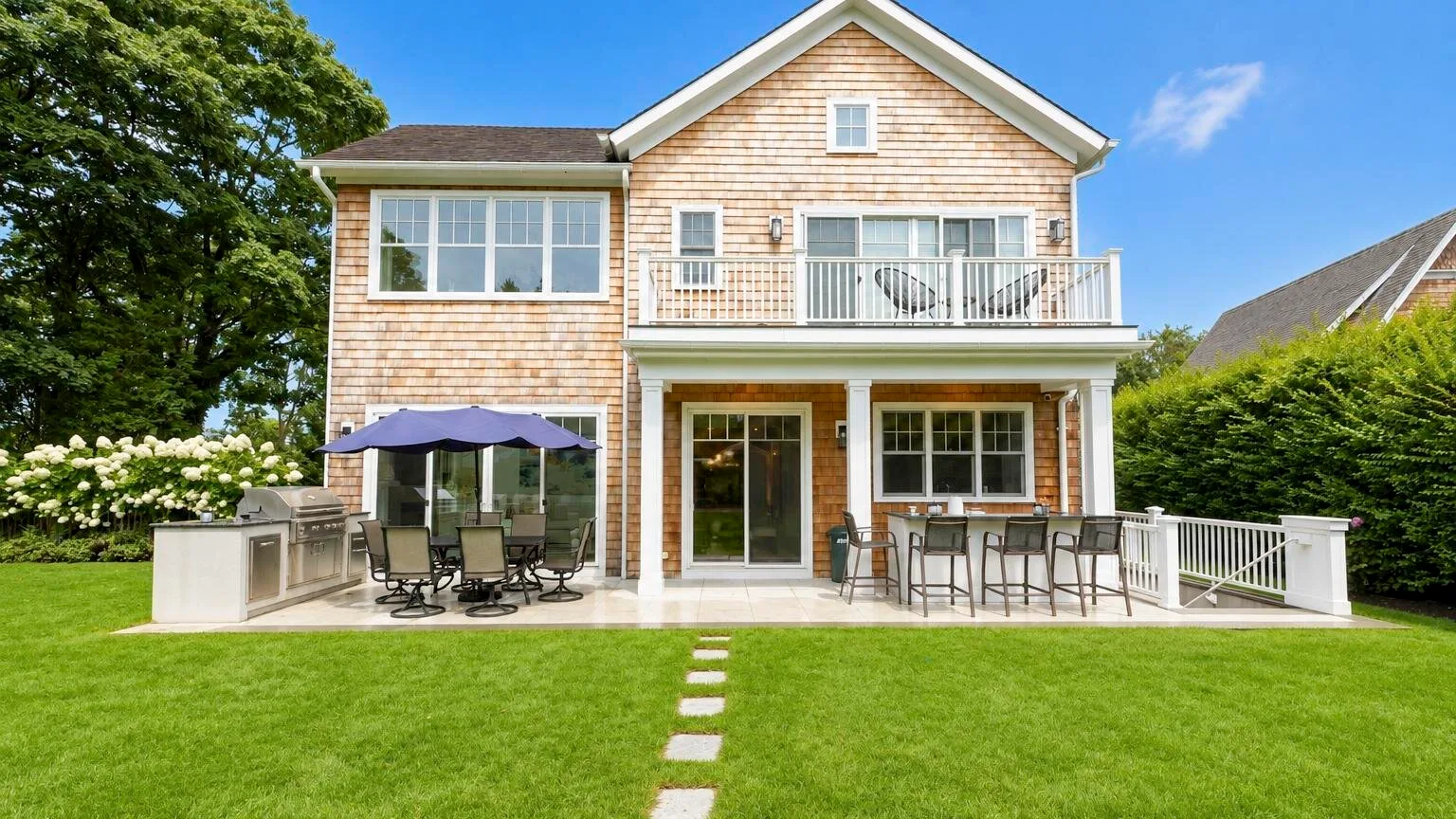 A two-story house with a lawn, patio seating, and an upper balcony.