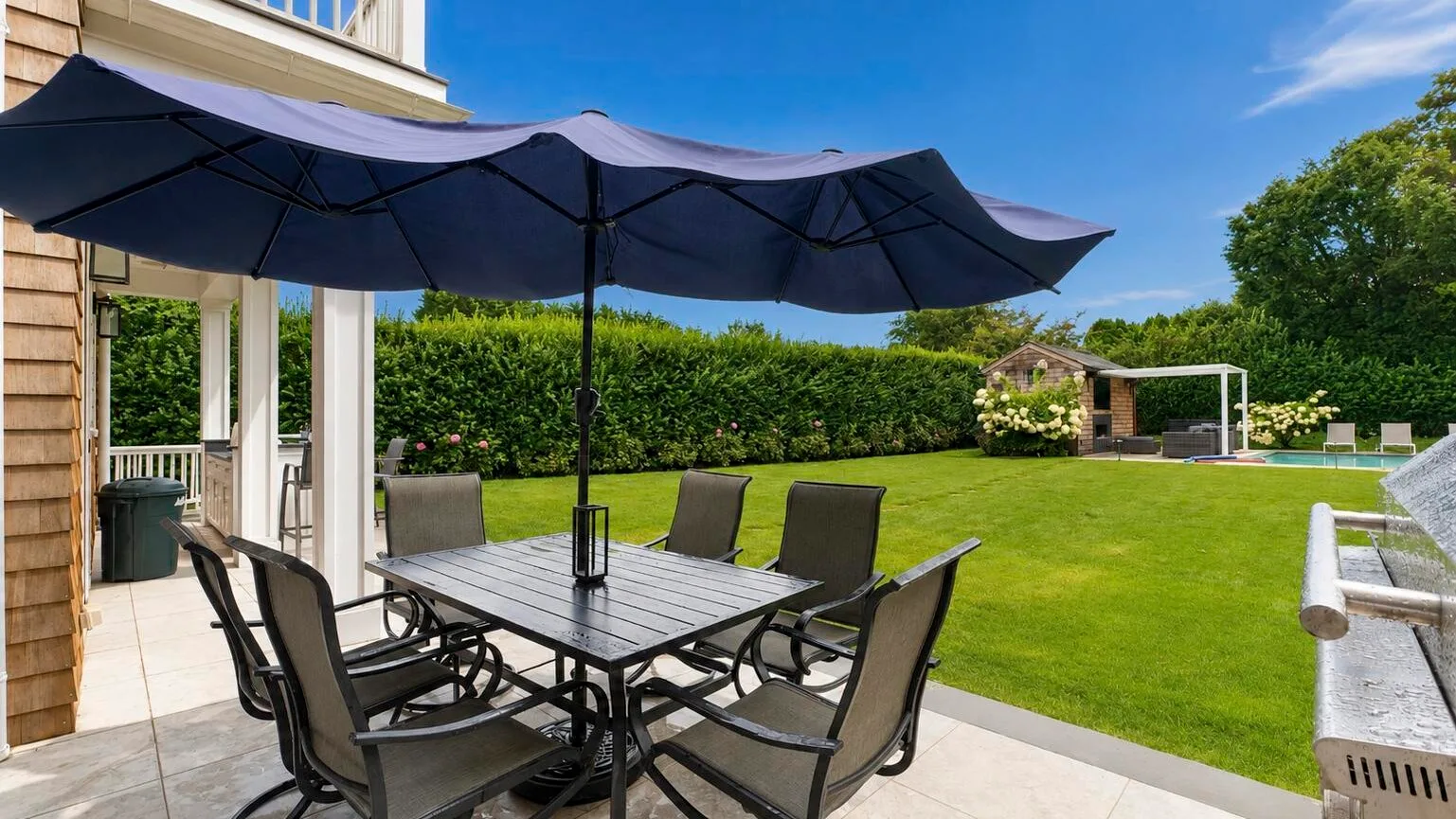 A patio dining area beneath large umbrellas overlooks a green lawn.