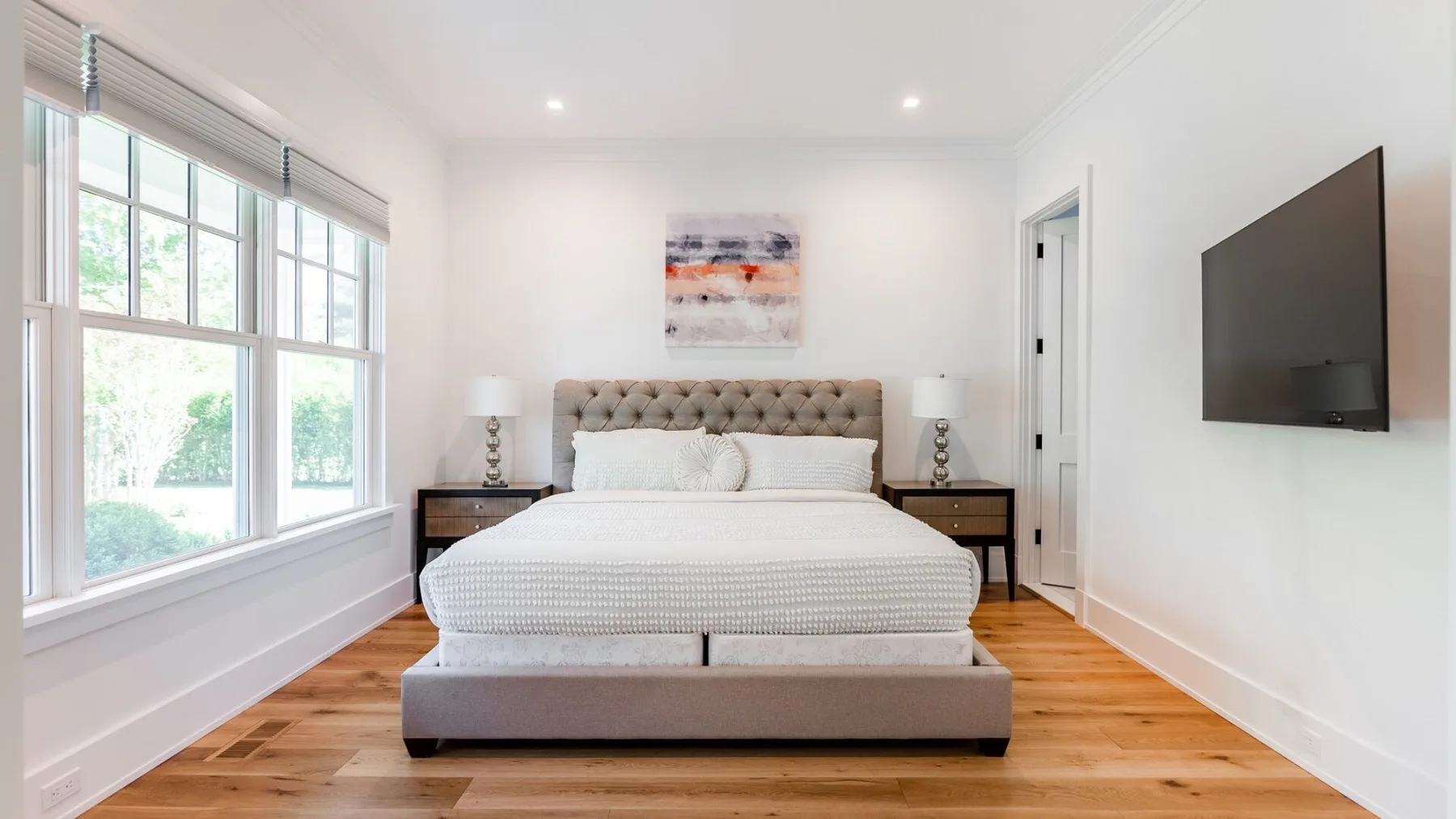 A bright bedroom with a neatly made bed and large windows.