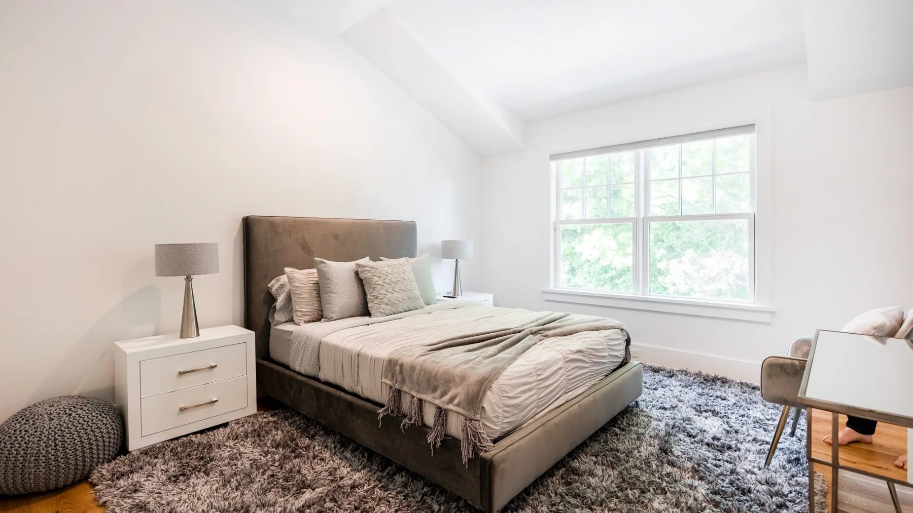 A bright bedroom with a neatly made bed and a large window.