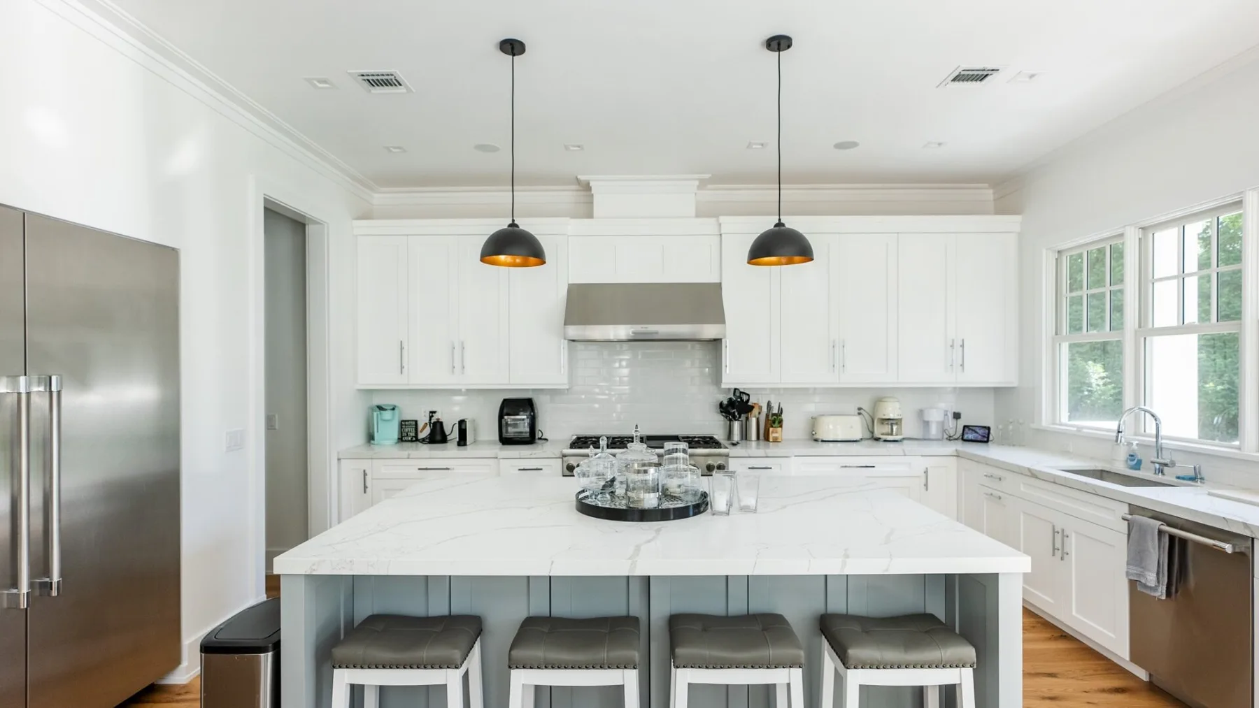 A bright white kitchen with a large island and pendant lights.