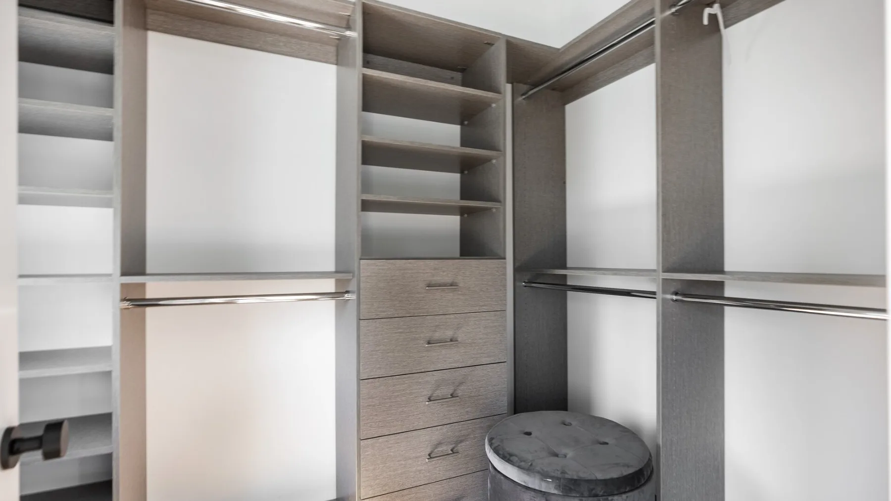 A walk-in closet with open shelving, drawers, and a small upholstered stool.