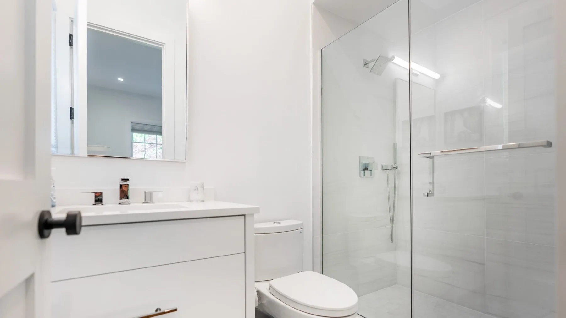 A bright bathroom with a vanity, mirror, and glass shower.