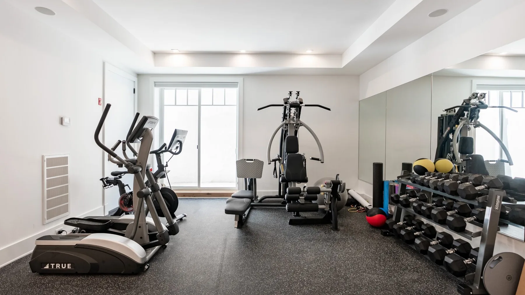 A bright exercise room with cardio machines and a rack of weights.