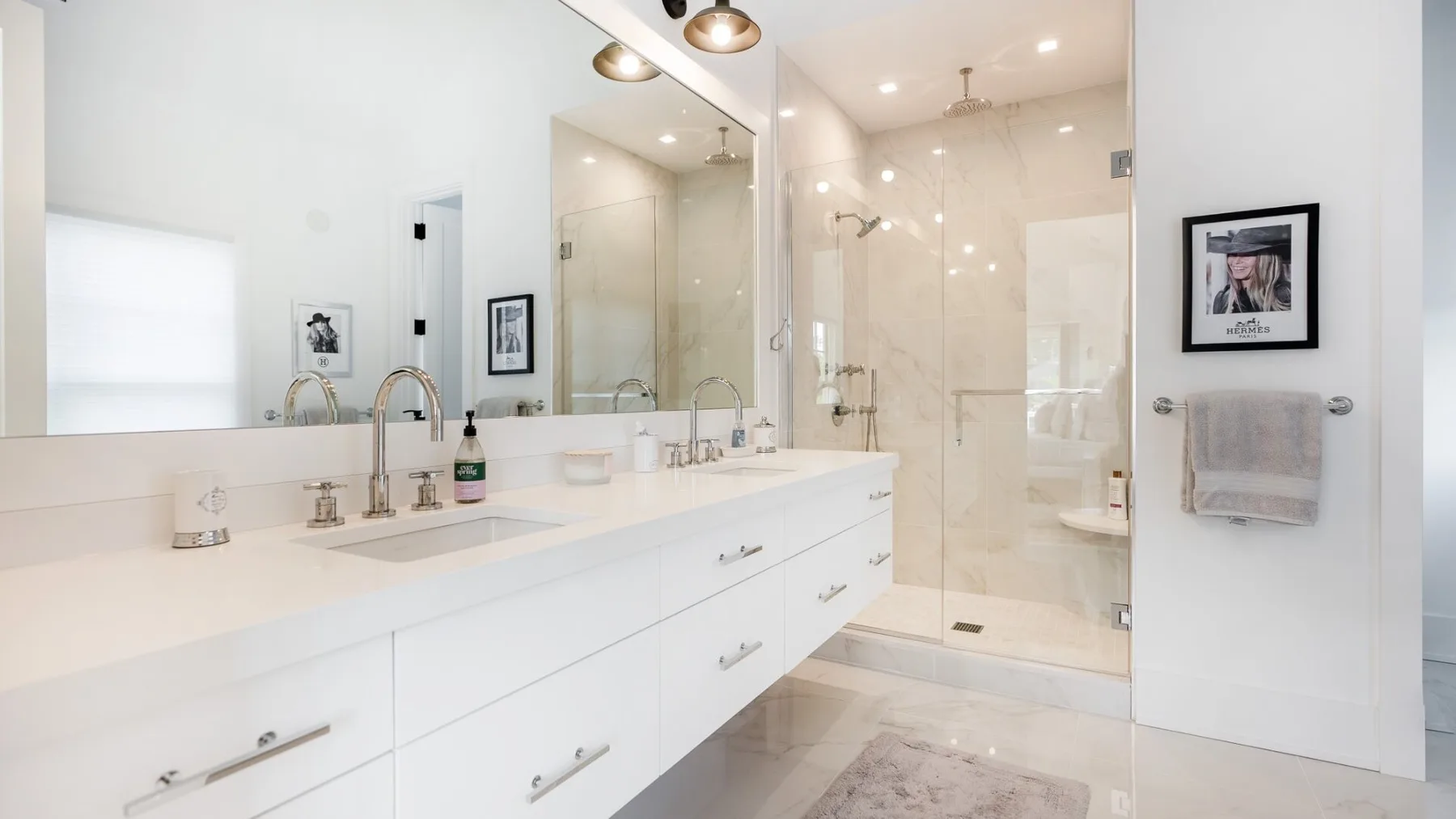 A bright bathroom with a long white vanity and a glass-enclosed shower.
