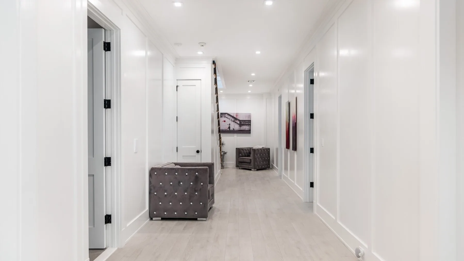 A bright white hallway with several doorways and a small seating area at the far end.