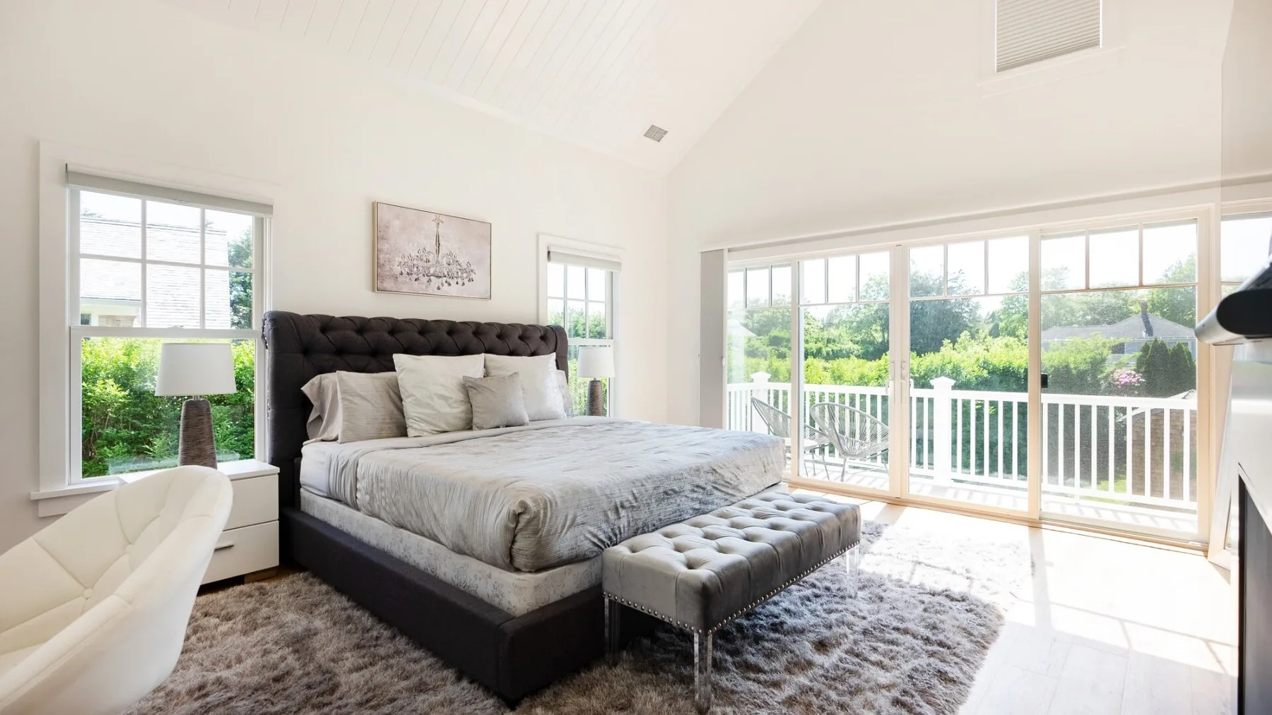 A bright bedroom with a large bed and tall windows overlooking greenery.
