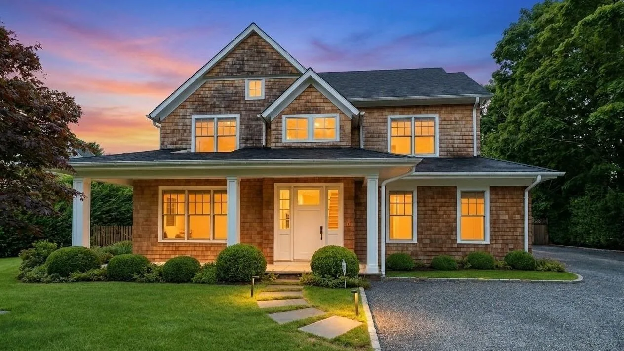 A two-story house with a covered front porch and illuminated windows at dusk.