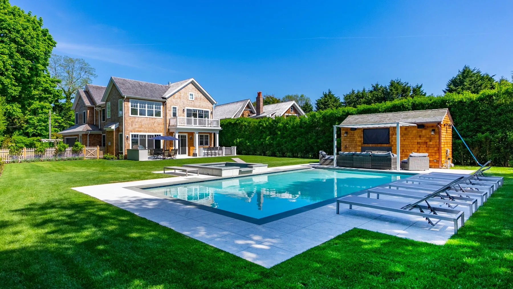 A landscaped backyard with a swimming pool beside a large house.