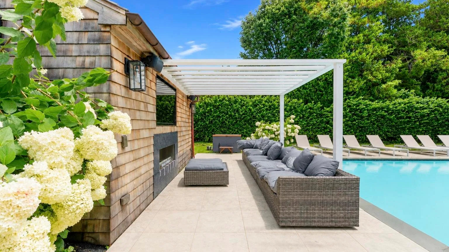 A poolside patio with cushioned seating beneath a white pergola.