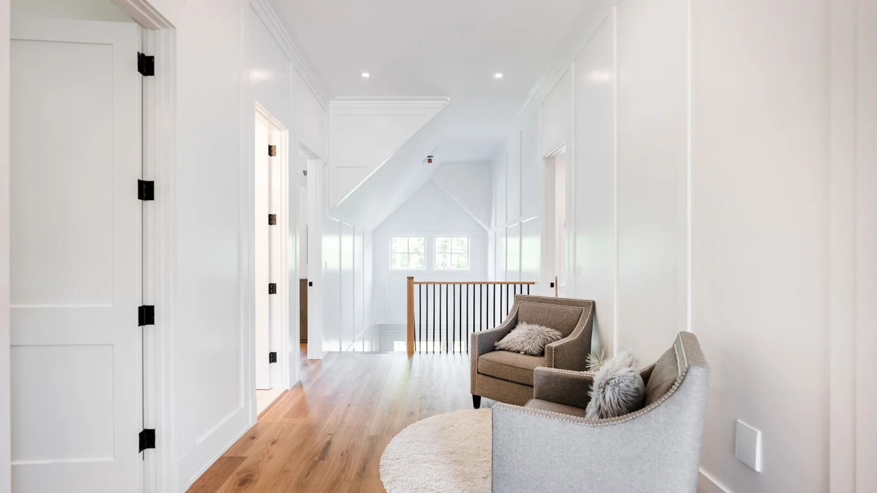 A bright upstairs hallway opens onto a landing with seating and a wooden floor.