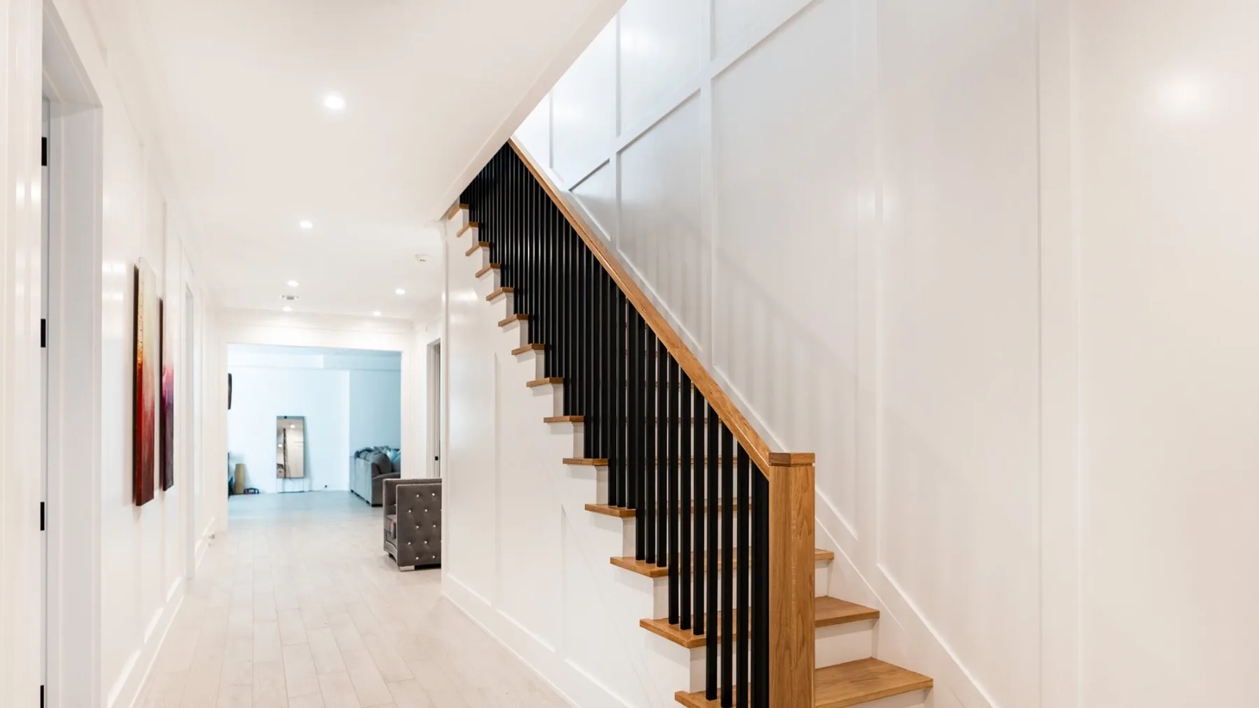 A bright hallway with a staircase and framed artwork along the wall.