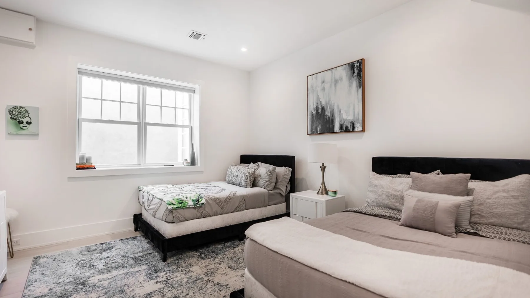 A bright bedroom with two beds, a large window, and wall art.