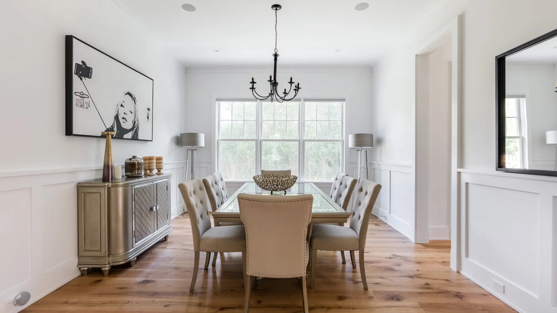 A bright dining room with a glass table and upholstered seating beneath a chandelier.