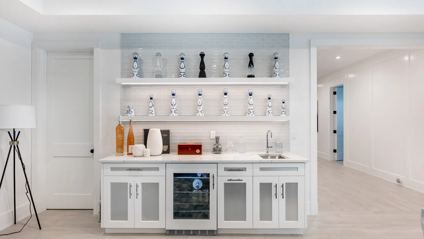 A bright white hallway features built-in cabinets, display shelves, and a beverage cooler.