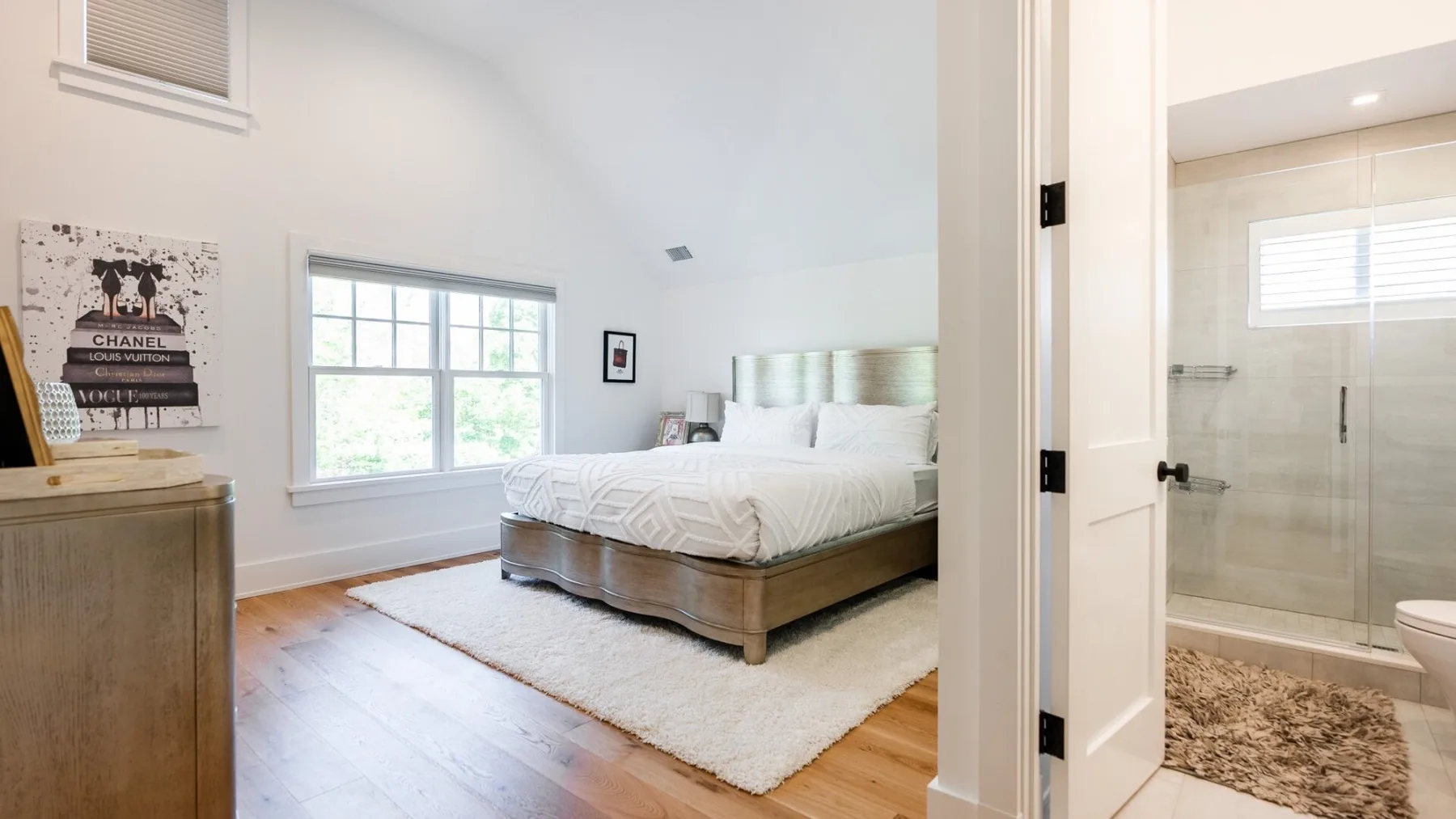 A bright bedroom with a bed beside a large window and an adjoining bathroom.