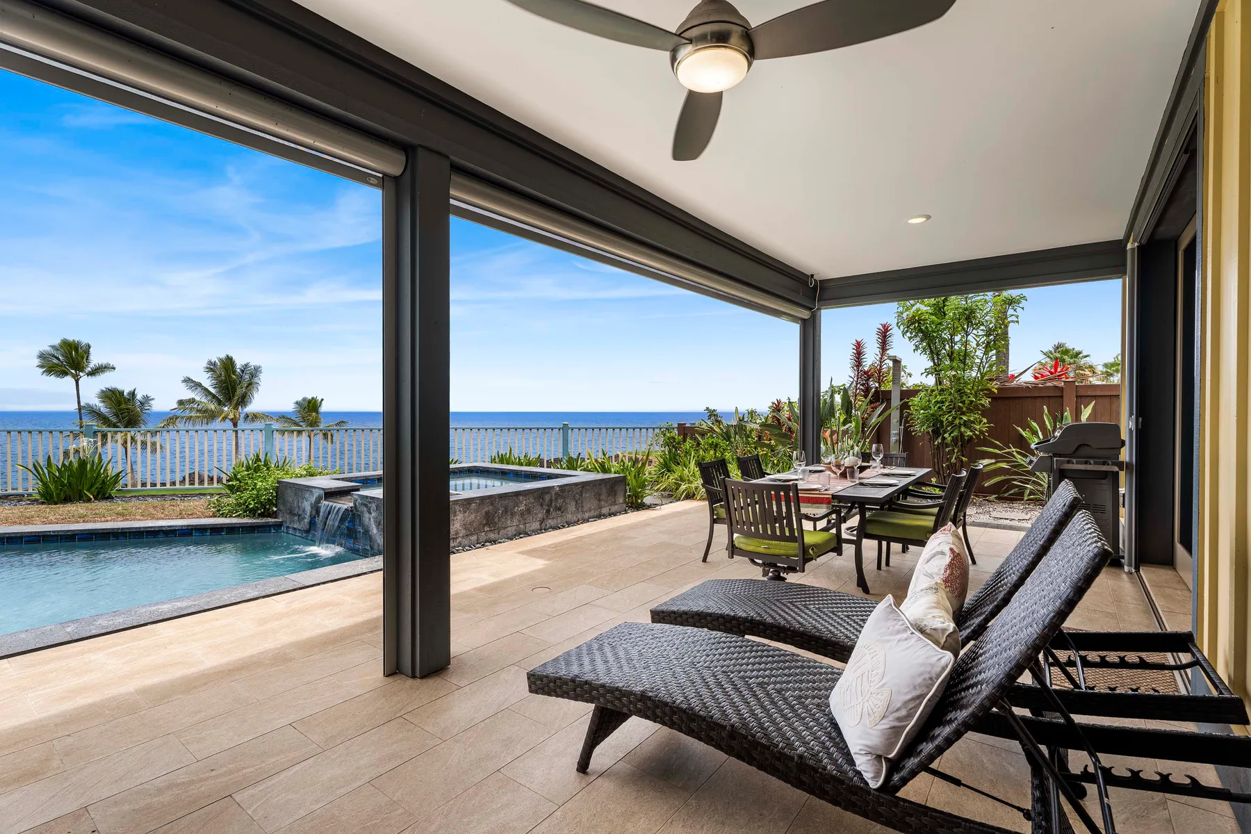 A covered patio overlooks a pool and the ocean, with outdoor seating and a dining table.