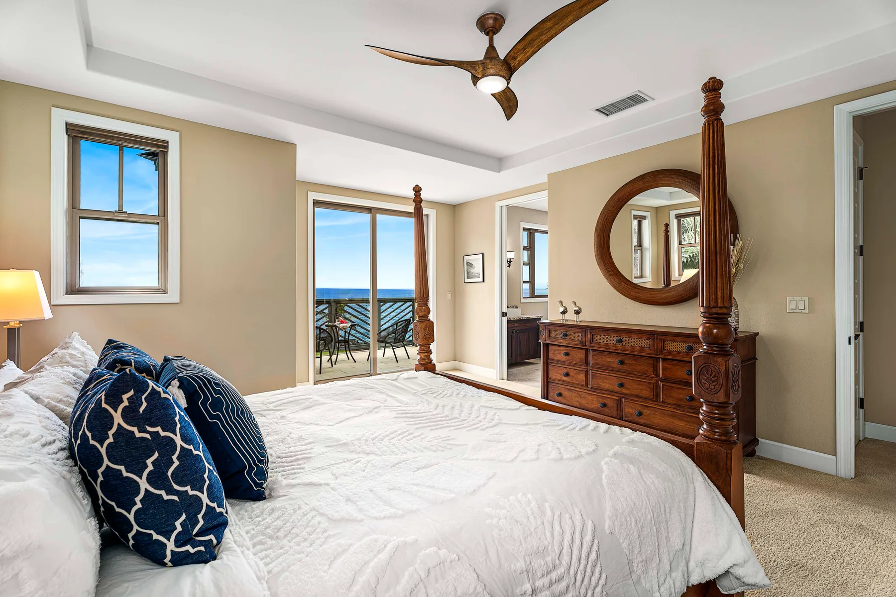 A bright bedroom with a large bed and a dresser topped by a round mirror.