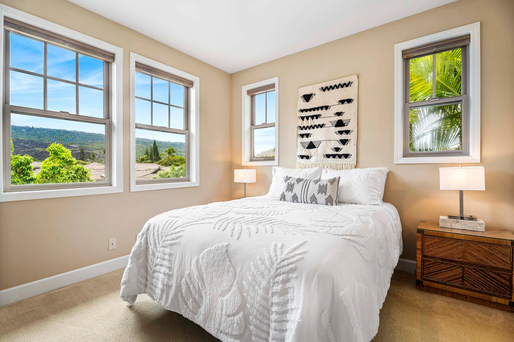 A bright bedroom with a white bed and several windows overlooking greenery.