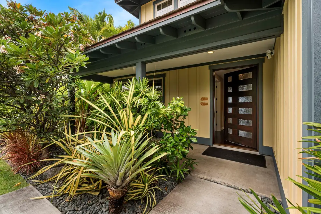 A covered building entrance with a dark wooden door and landscaped plants.