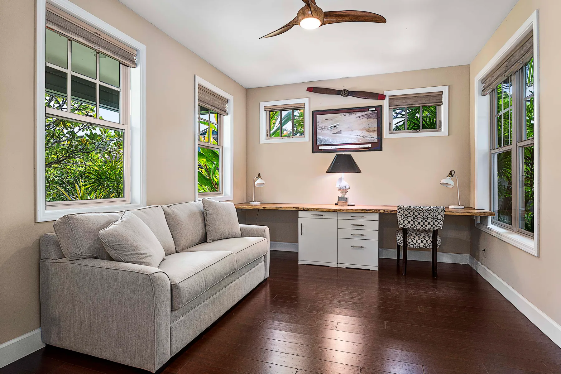 A small living room with a sofa and a desk beneath several windows.
