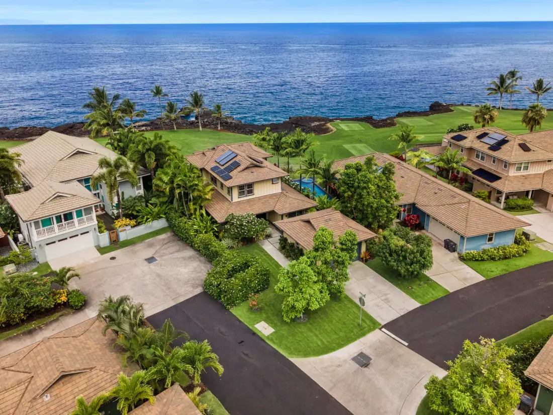 Aerial view of coastal homes beside a green lawn and the ocean.