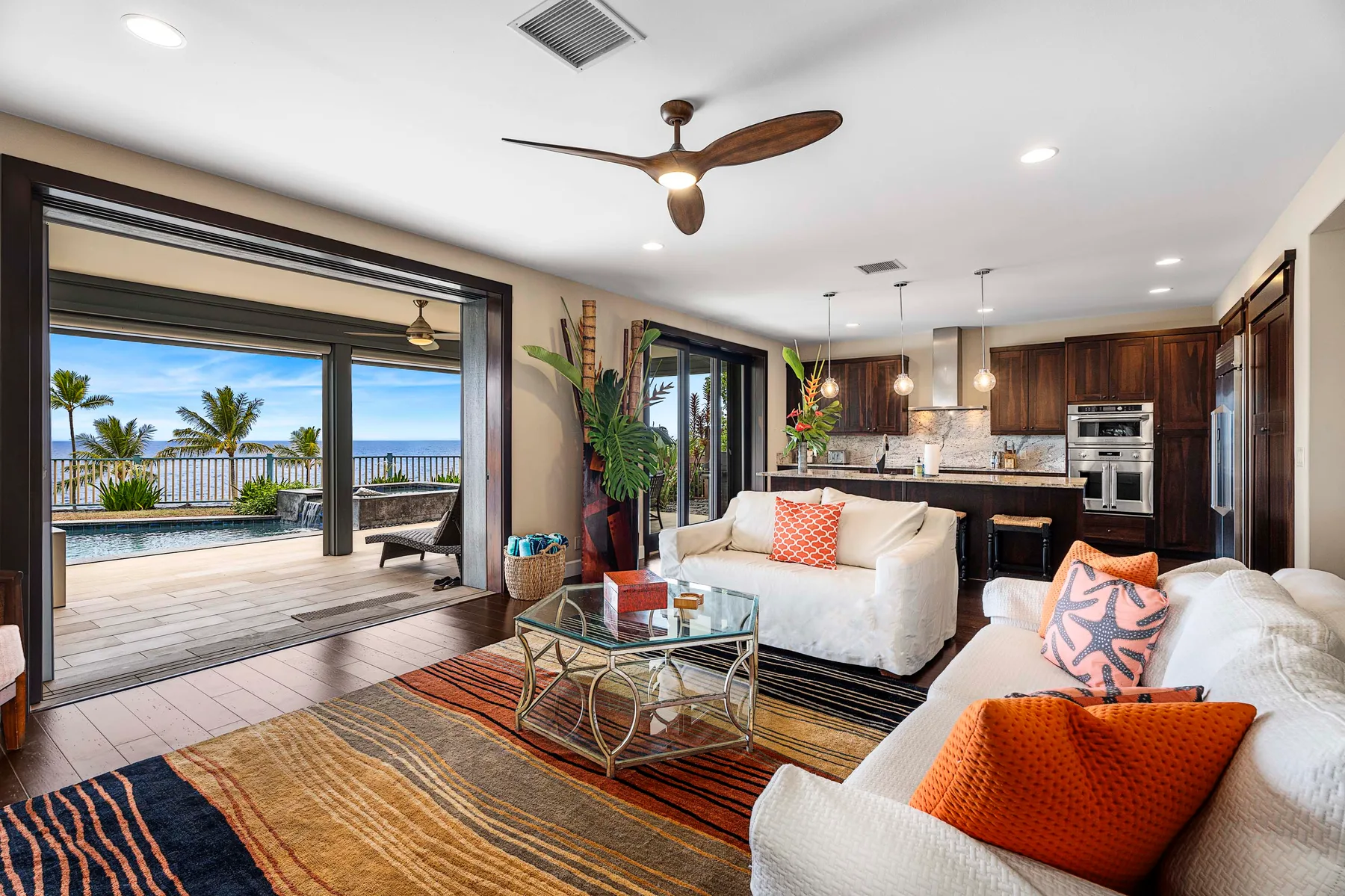 A living room opens onto a patio, with a kitchen visible in the background.