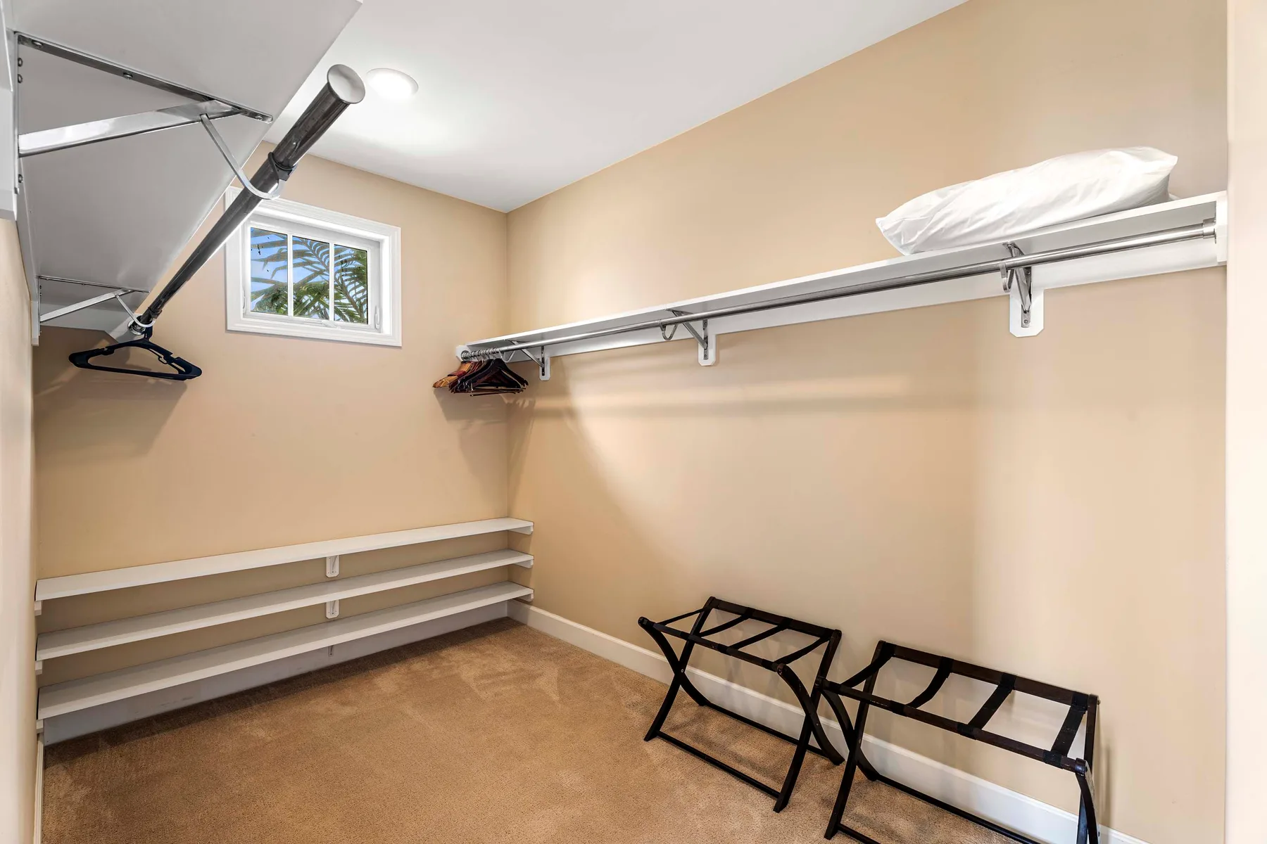 A walk-in closet with open hanging rails and shoe shelves.