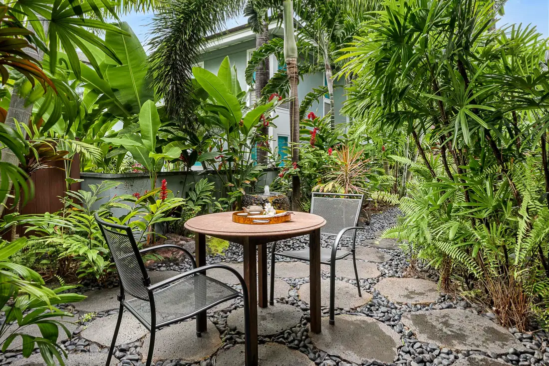 A garden patio with a round table and seating among lush tropical plants.