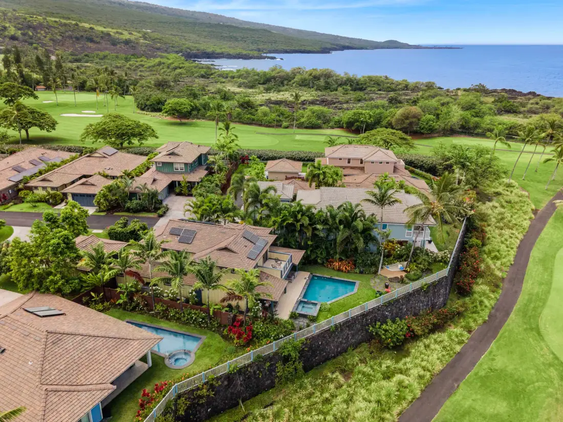 Aerial view of homes with gardens and a swimming pool beside a golf course.