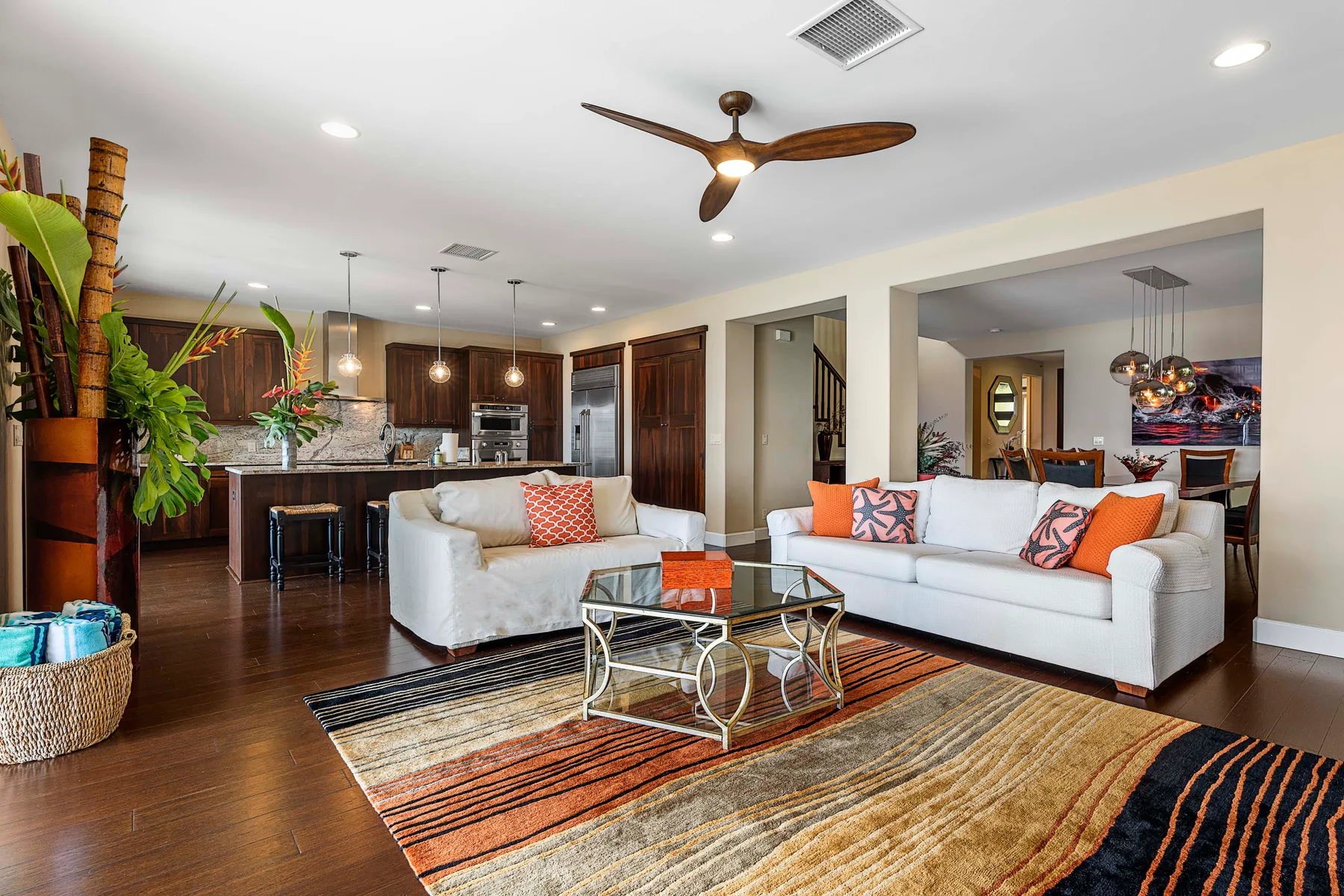 A bright living room with white seating, a glass coffee table, and an open kitchen.