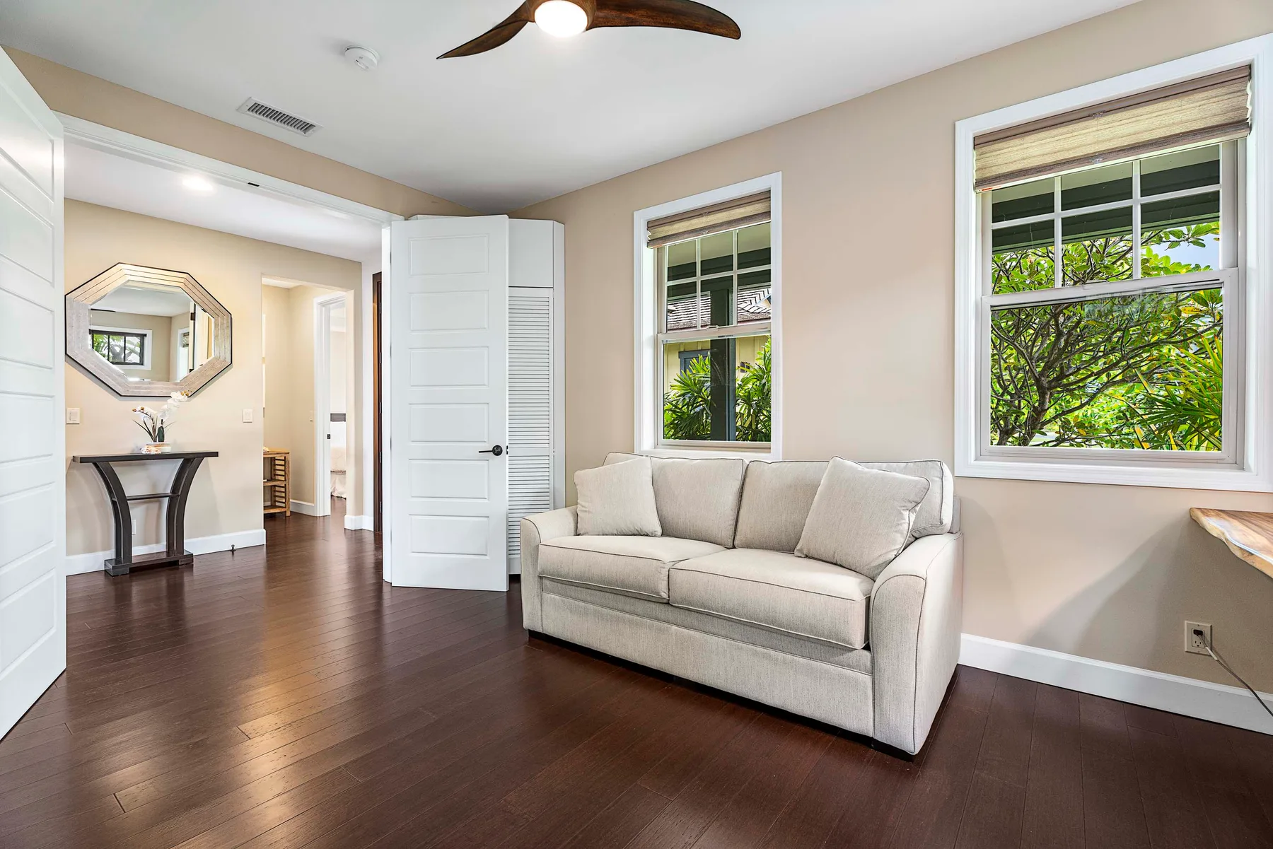 A bright sitting area with a light sofa, two windows, and dark wood flooring.