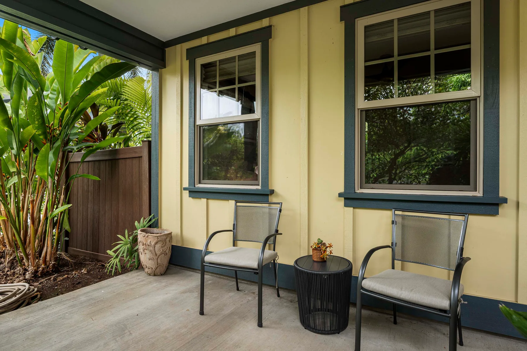 A covered patio with two chairs beside windows and tropical plants.