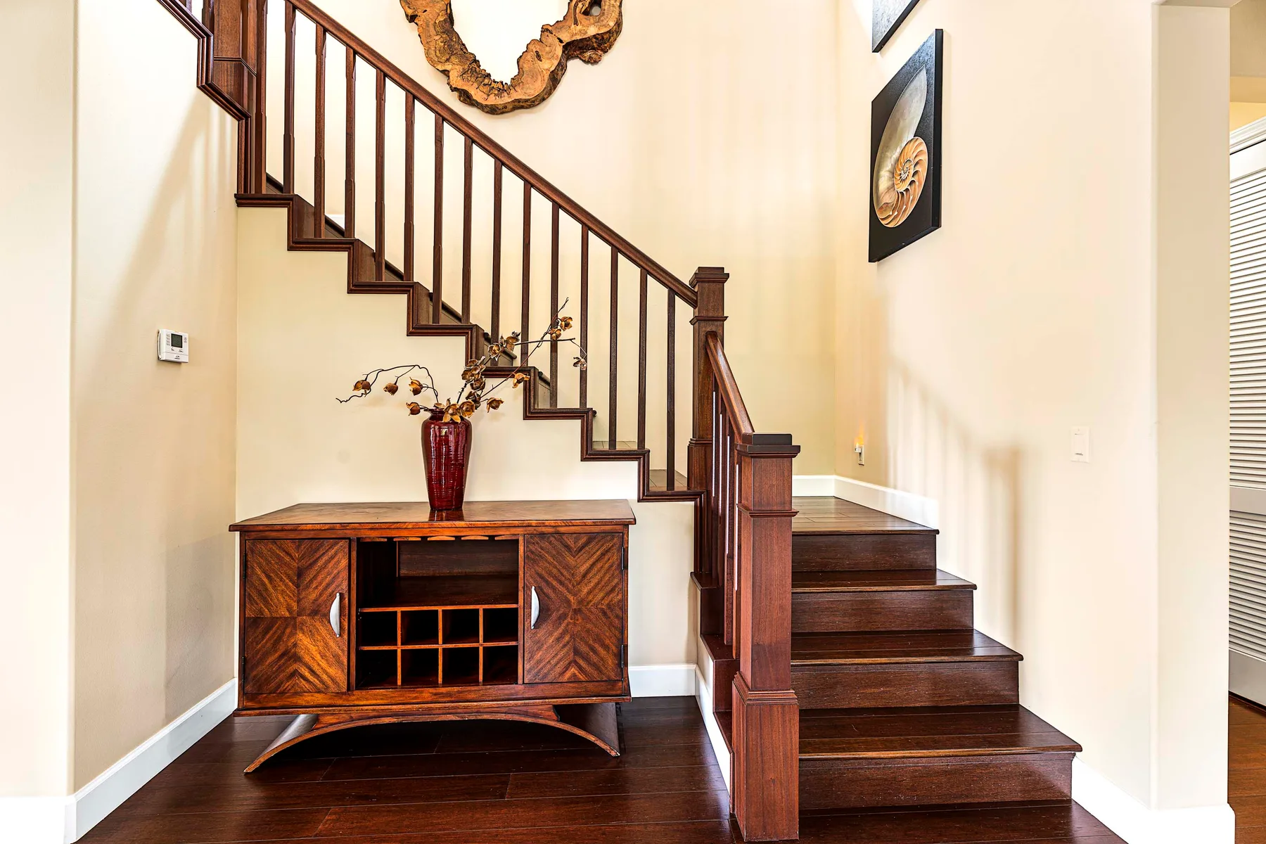 A wooden staircase rises above a console table in a bright interior.