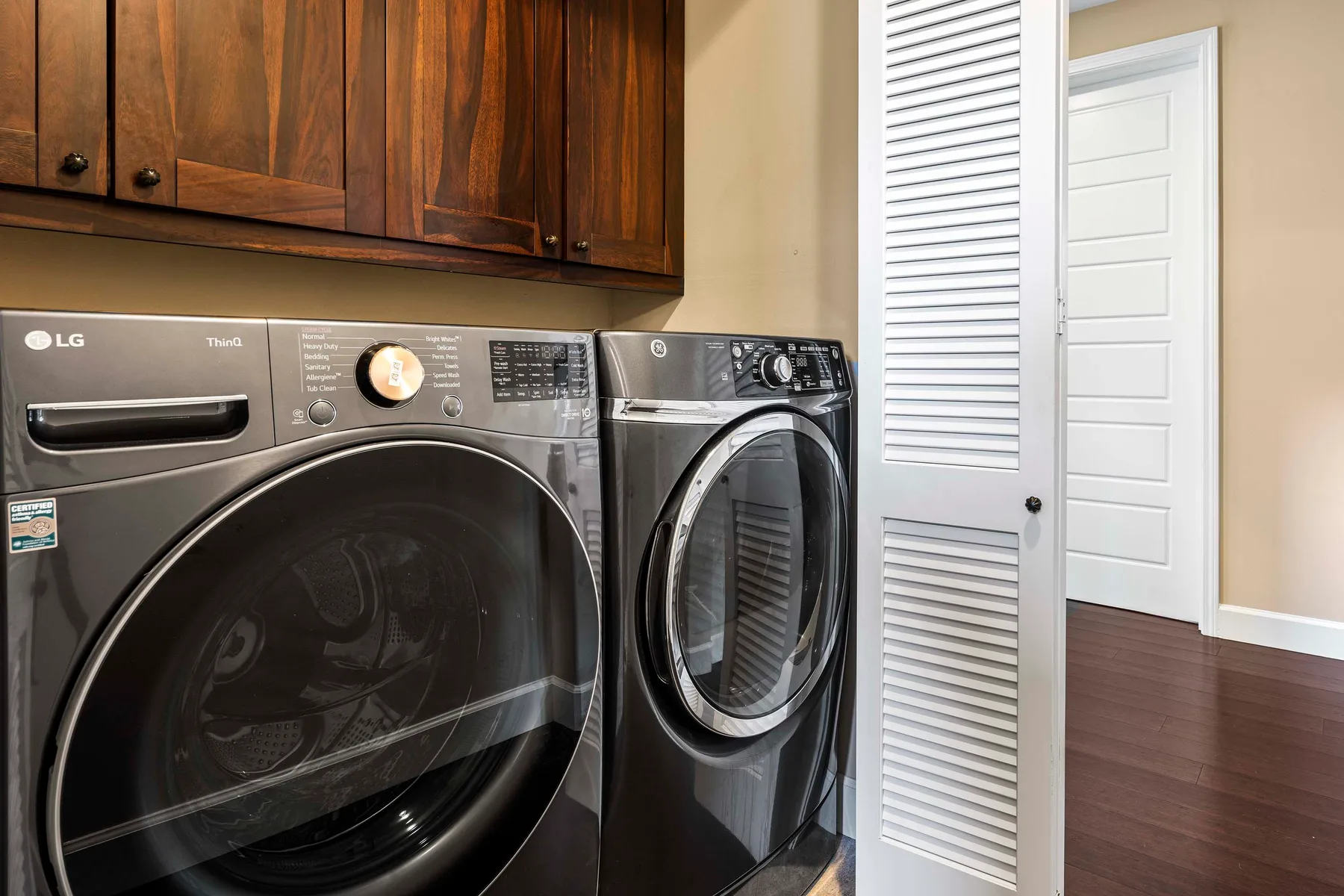 A laundry area with front-loading washer and dryer beneath dark wood cabinets.