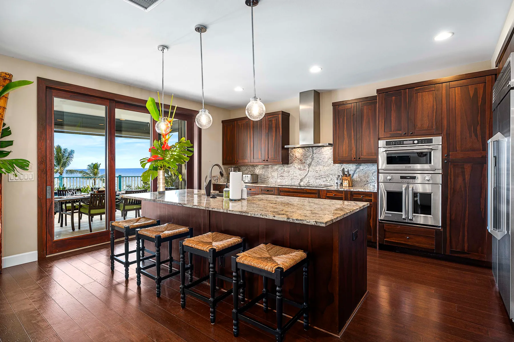A spacious kitchen with a large island, dark cabinets, and glass doors opening to a patio.