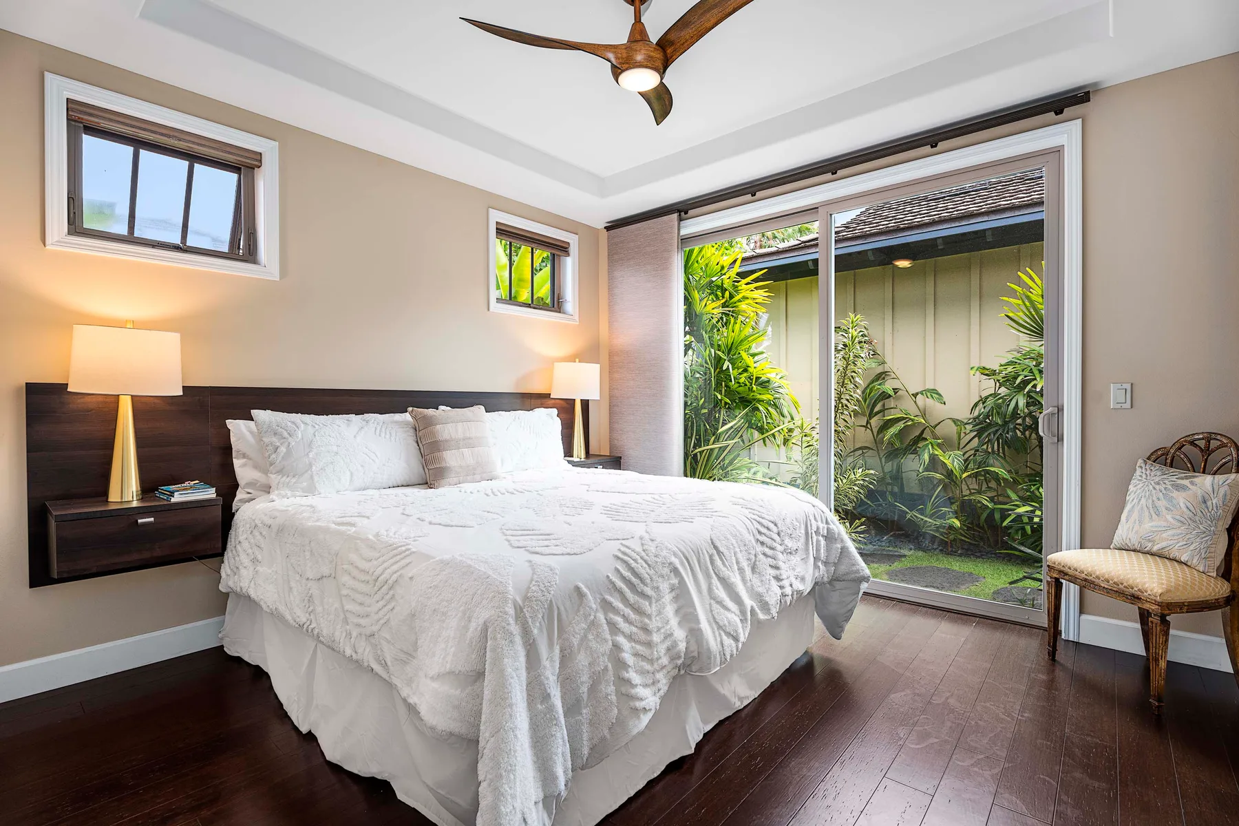A bedroom with a large bed beside sliding glass doors opening onto a leafy patio.