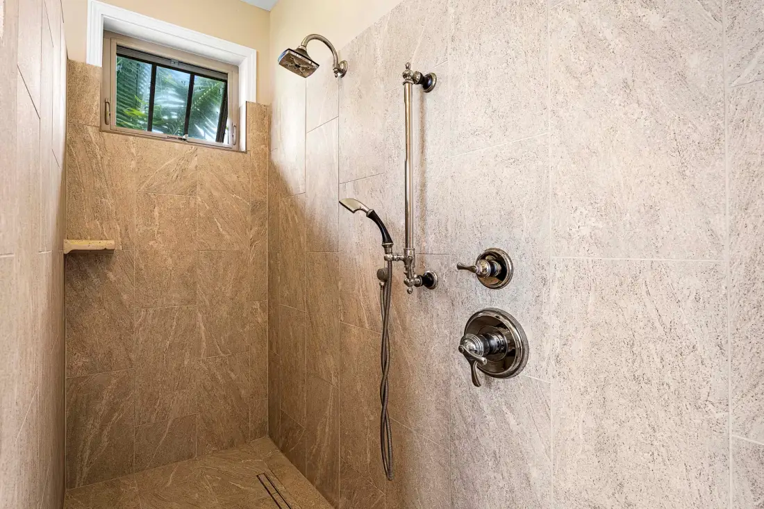 A tiled shower with a handheld showerhead and a small window.