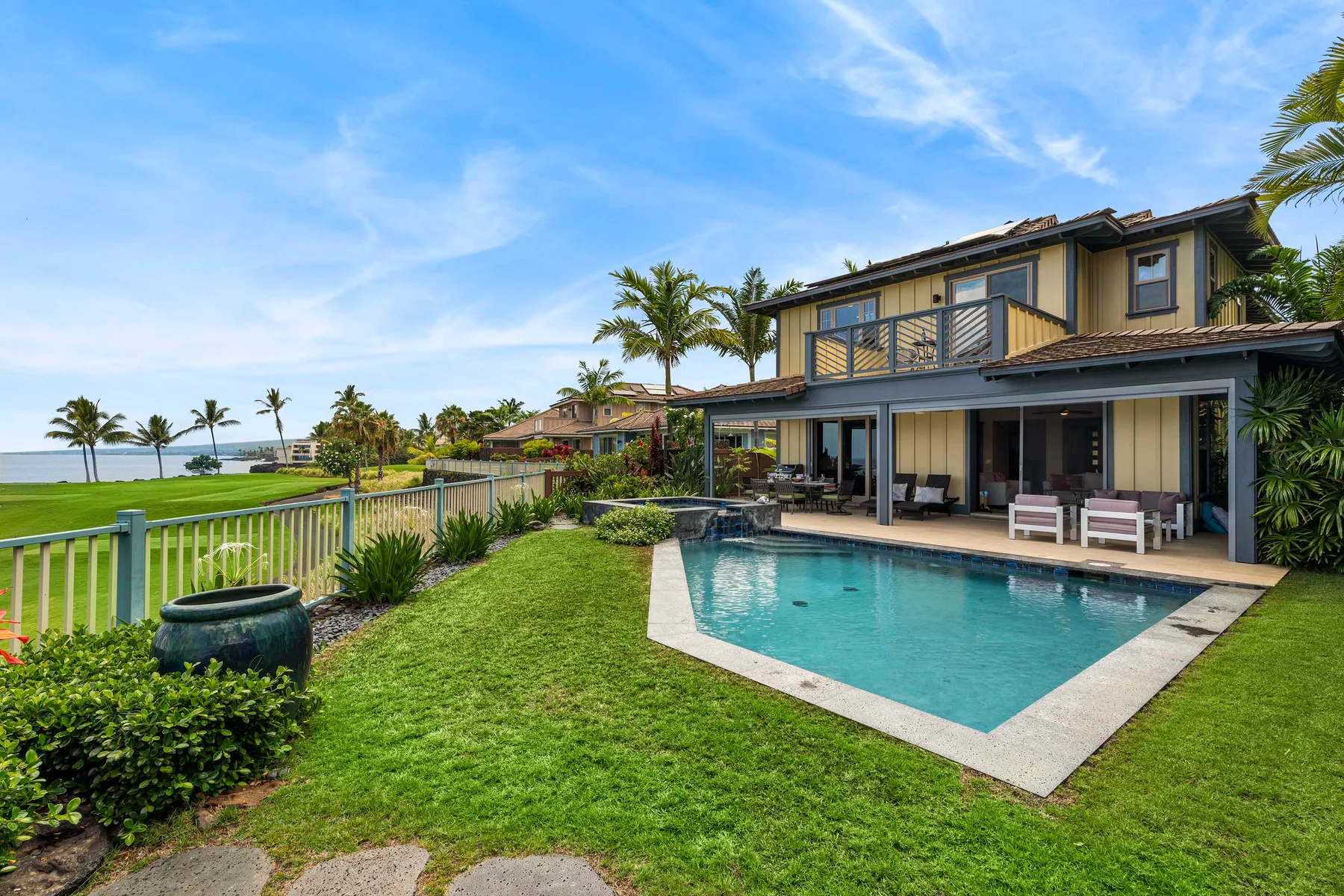 A coastal home with a swimming pool, lawn, and ocean view.