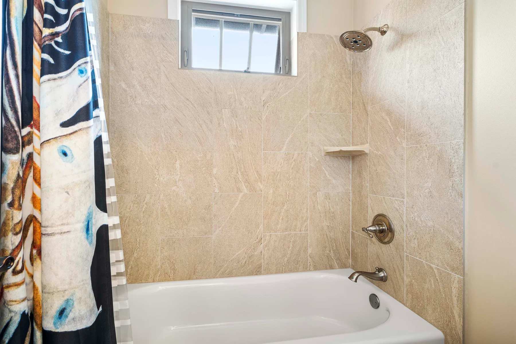 A tiled bathroom with a bathtub, showerhead, and colorful shower curtain.
