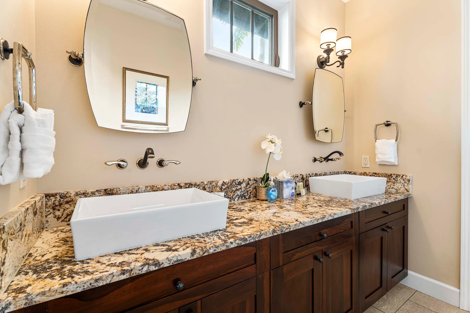 A bathroom vanity with two sinks, stone countertops, mirrors, and wall lights.