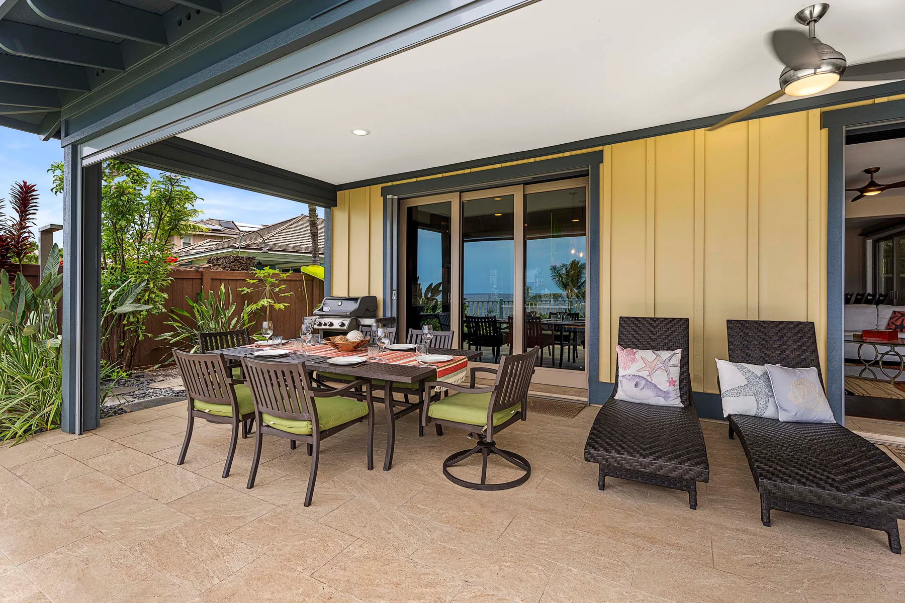 A covered outdoor patio with dining seating and lounge chairs beside glass doors.