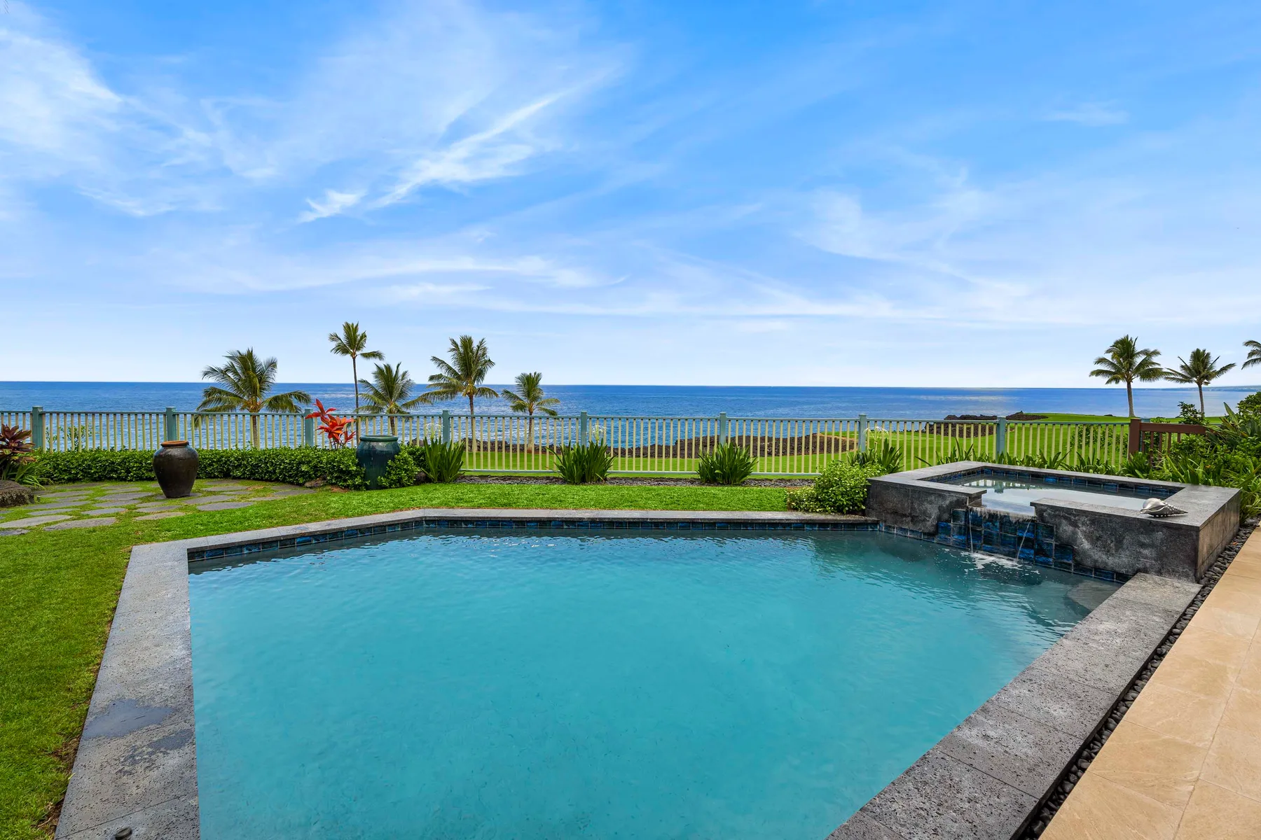 A swimming pool overlooks a grassy lawn and the ocean.