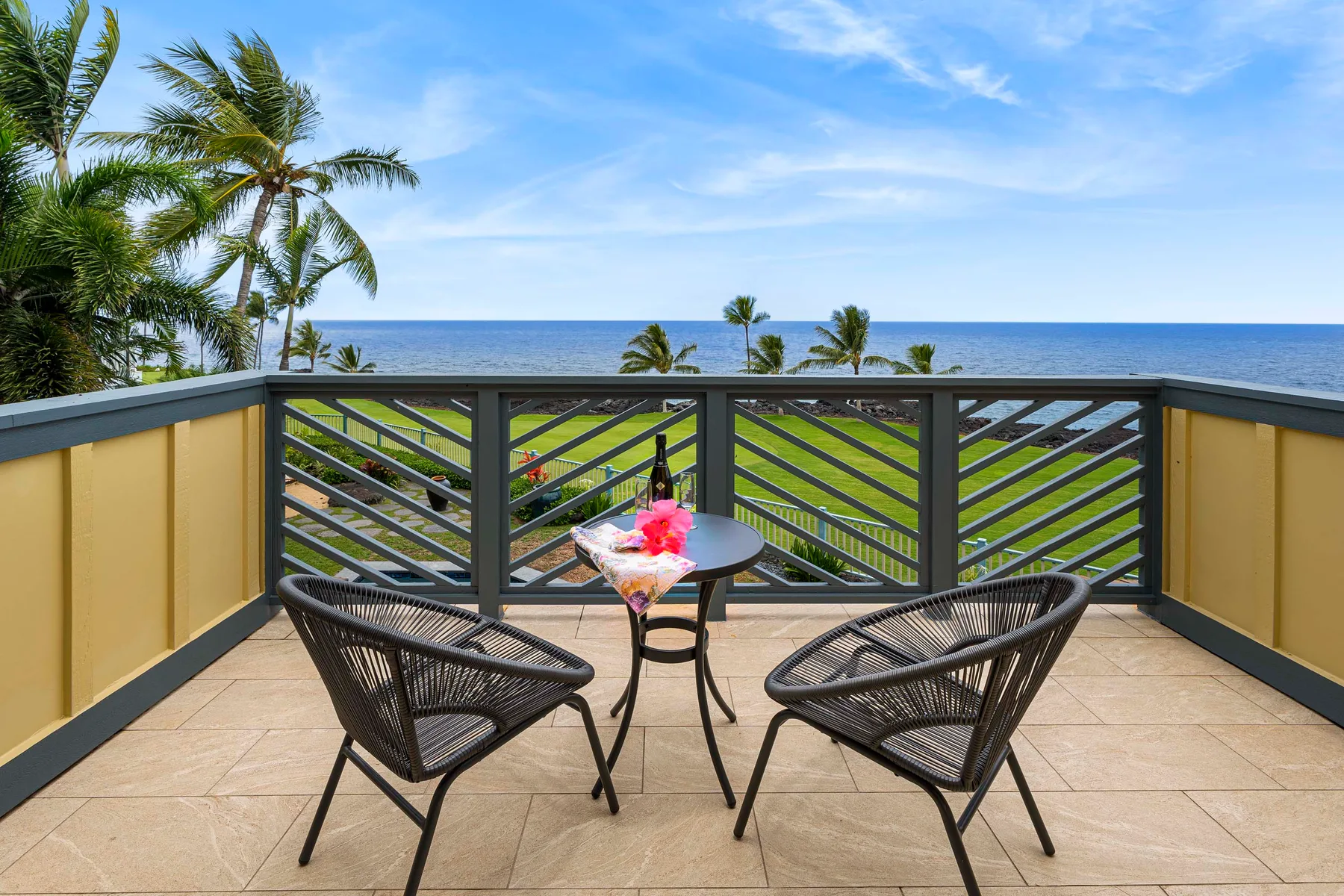 A seaside balcony with two chairs and a small table overlooks the ocean.