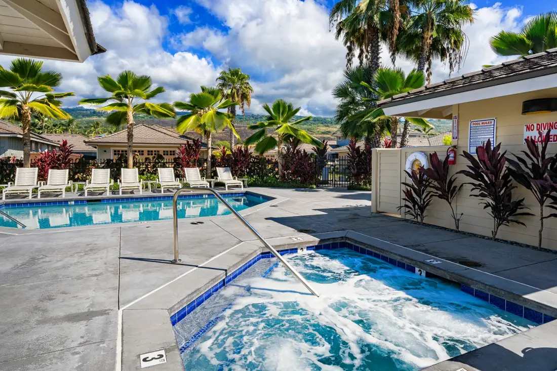 A swimming pool and bubbling spa sit in a sunny outdoor courtyard with palm trees.