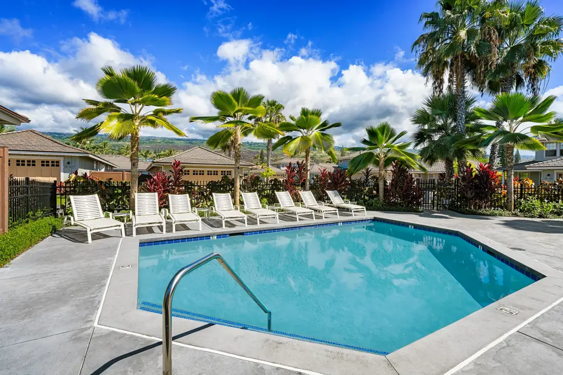 An outdoor swimming pool is surrounded by lounge seating and palm trees.