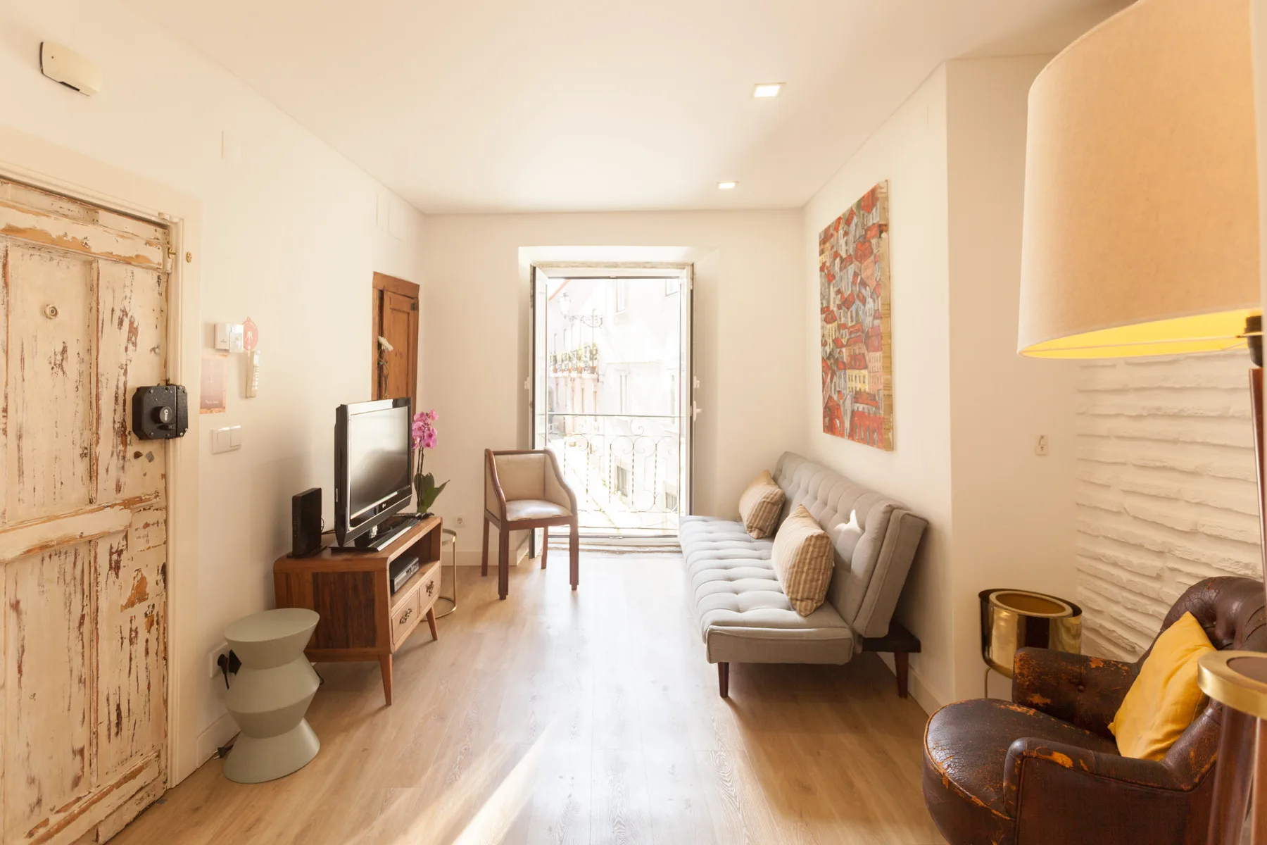 Una sala luminosa con asientos, un televisor y una puerta de balcón.