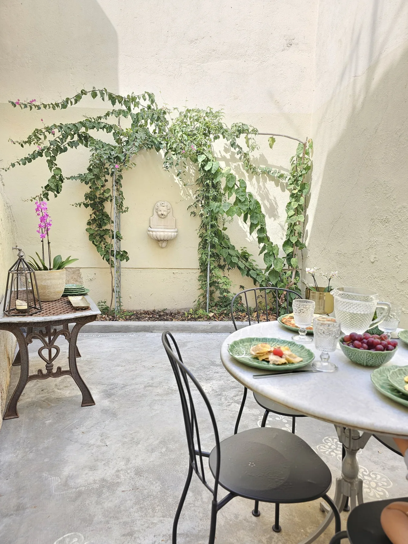 Un comedor soleado en un patio tiene una mesa redonda con platos y tazas.