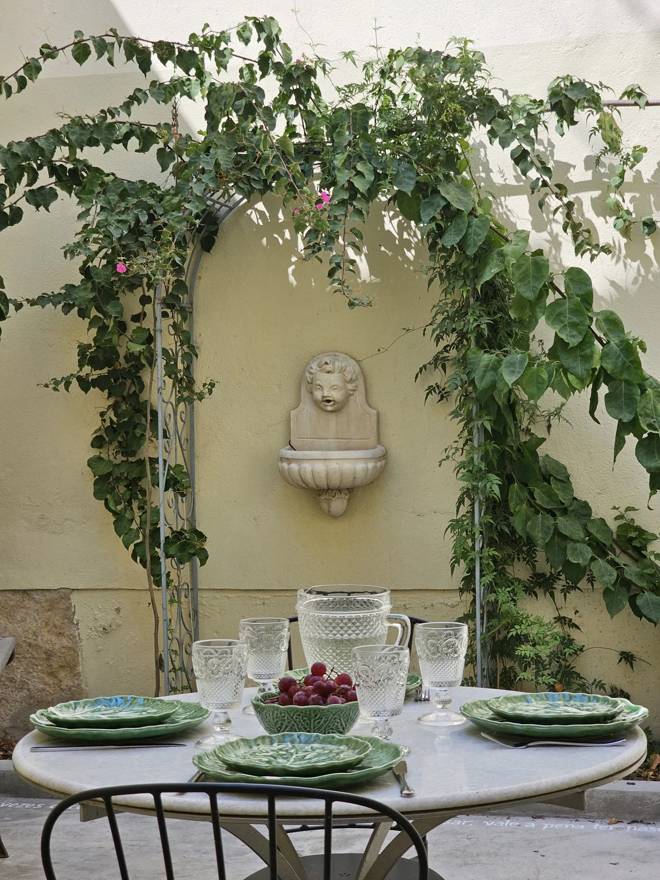 Comedor de jardín con una mesa puesta bajo enredaderas frondosas.
