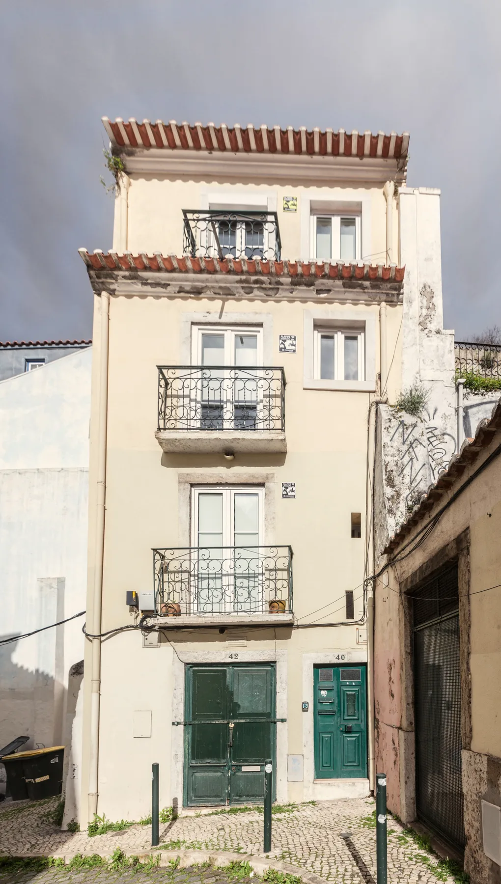 Un edificio residencial estrecho con balcones y puertas verdes a nivel de calle.
